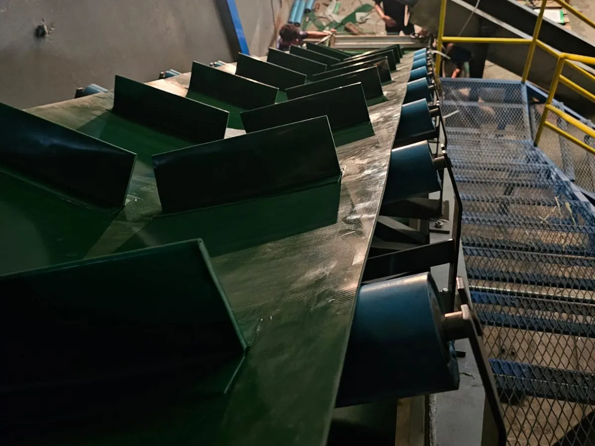 Conveyor miring dengan sekat cleat hijau tua dan pagar pengaman di dalam pabrik pelanggan