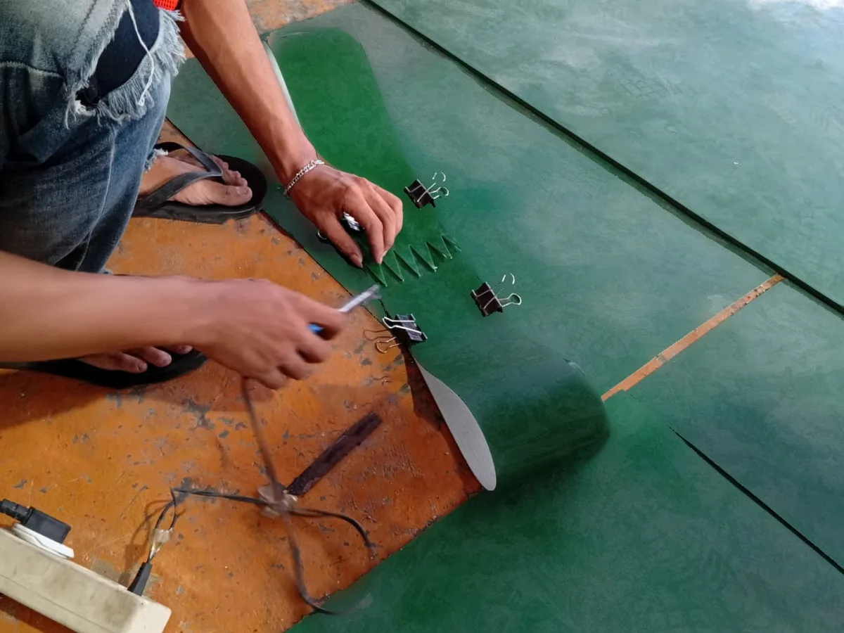 Teknisi menyiapkan sambungan belt PVC hijau di atas plat press, jari-jari sambungan dijepit binder clip sebelum dipanaskan