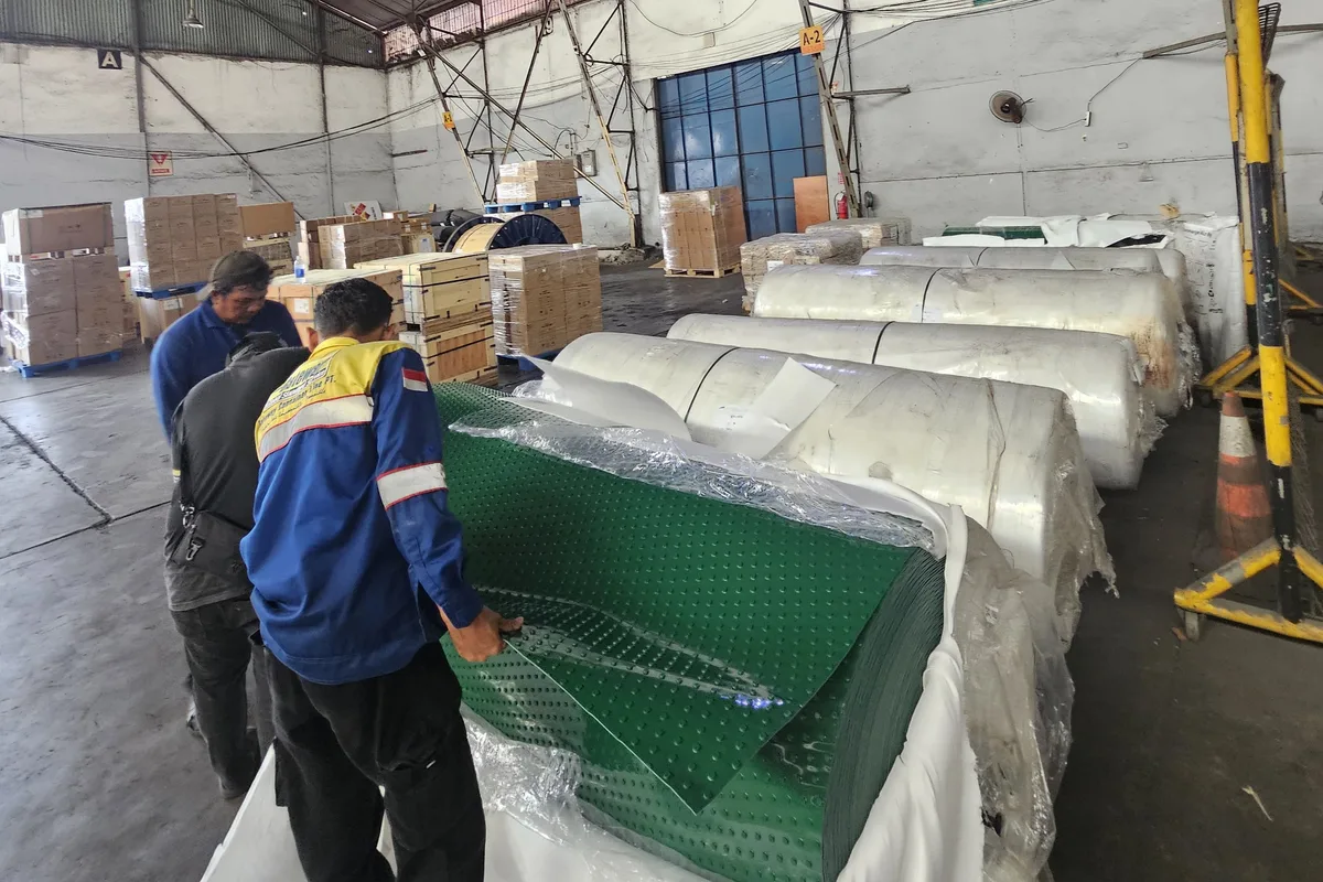 Dua kru BBS membentangkan belt PVC hijau bertekstur di antara gulungan belt terbungkus di workshop Pulo Gebang